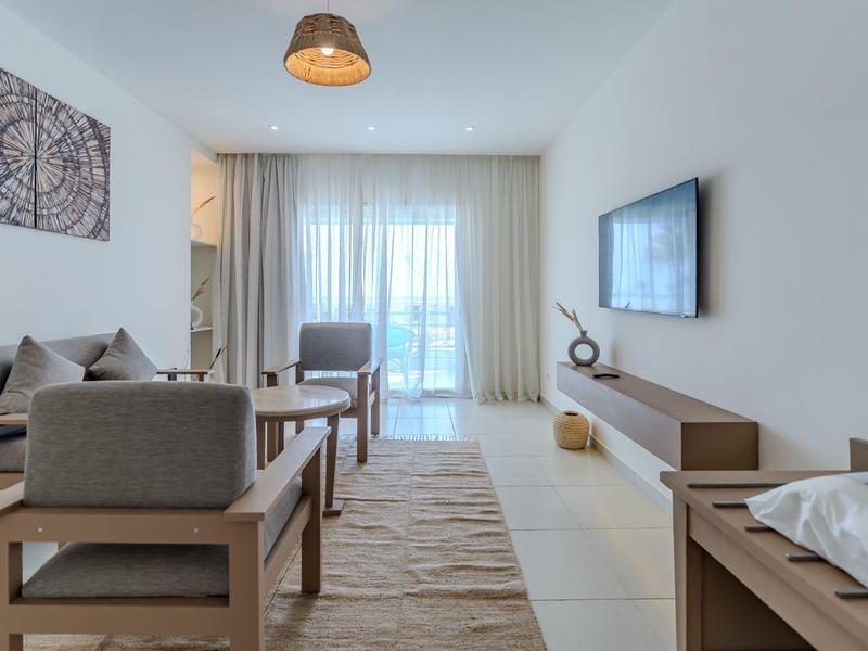 Moderně zařízený hotelový pokoj s posezením, televizí a velkým oknem s závěsy.