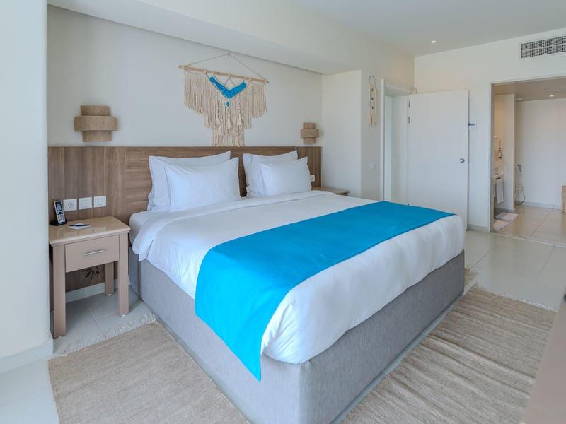 Moderní hotelový pokoj s velkou postelí, dřevěnými detaily a světlou, přívětivou atmosférou.