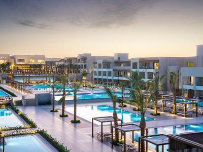 Moderner Hotelpoolbereich mit mehreren Pools, Palmen und beleuchteten Wegen bei Dämmerung.