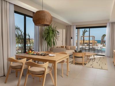 Moderner Hotelwohnraum mit Esstisch, gemütlichen Stühlen und Blick auf Terrasse und Meer.