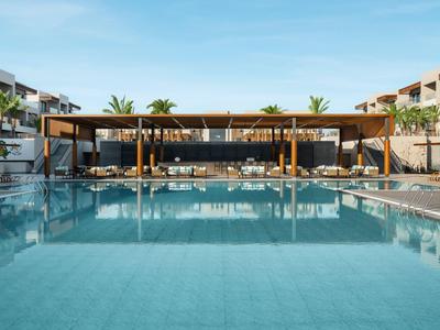 Moderner Hotelpool mit Liegestühlen und Poolbar unter klarem Himmel.