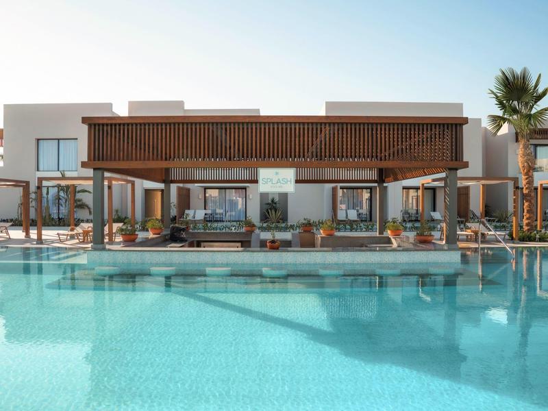 Edificio moderno dell'hotel con una grande piscina davanti sotto un cielo azzurro chiaro.