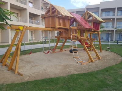 Holzspielplatz mit Rutsche, Schaukeln, Kletterseil und Sandfläche in einem Innenhof.