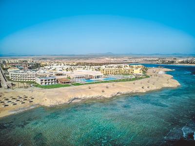 Küste mit klarem türkisfarbenem Wasser, Sandstrand, Hotels und Gebäuden unter blauem Himmel.