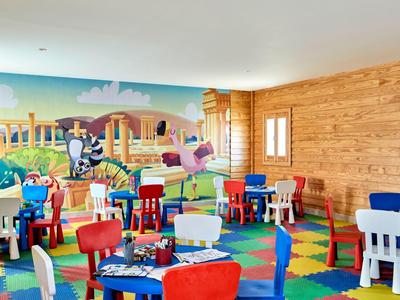 Bunter Kinderspielraum mit Holzverkleidung, Spielteppich und kindgerechten Tischen und Stühlen.
