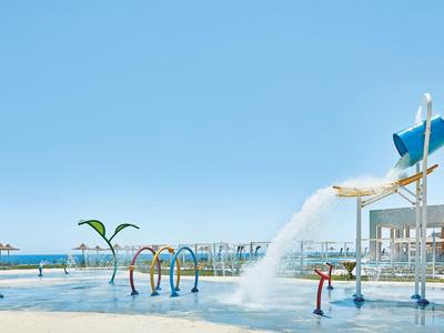 Wasserpark mit bunten Wasserspielen, großem Eimer, der Wasser schüttet, und klarem blauen Himmel.
