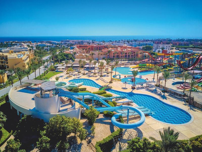 Vista aérea de un parque acuático con varias piscinas, toboganes y sombrillas bajo un cielo despejado.