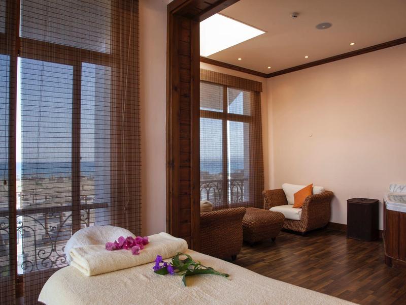 Klidný pokoj s masážním lehátkem, křesly a výhledem na moře přes velké okno.