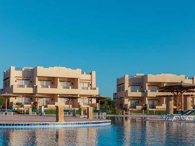 Edificios modernos de hotel con piscina, cielo azul y sombrillas en un complejo vacacional.