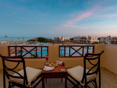 Balcón con mesa y dos sillas con vista a la piscina y edificios del hotel al atardecer.