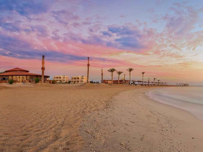 Strand mit feinem Sand, Palmen und bunter Abenddämmerung über ruhigem Meer.