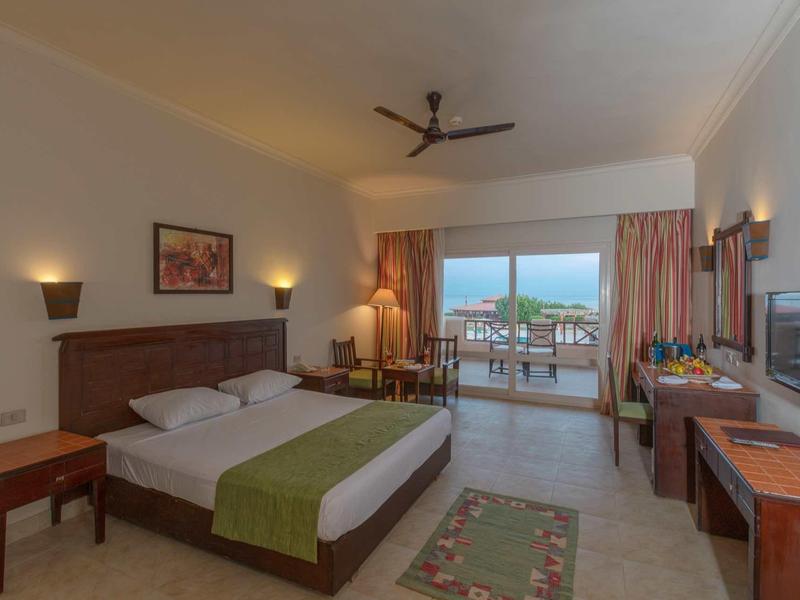 Geräumiges Hotelzimmer mit Doppelbett, Balkon, Deckenventilator und warmem Licht.