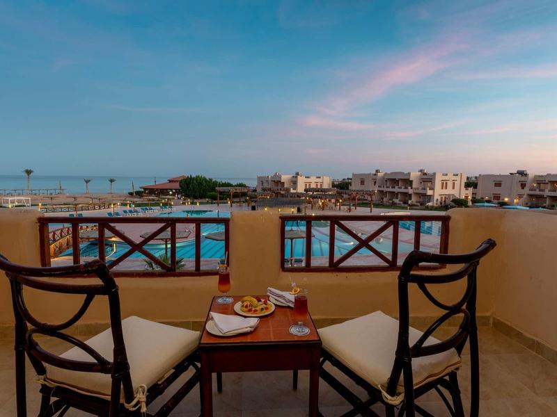 Terrassenblick auf Pool, zwei Stühle mit Kissen und Tisch mit Frühstück bei blauem Himmel.