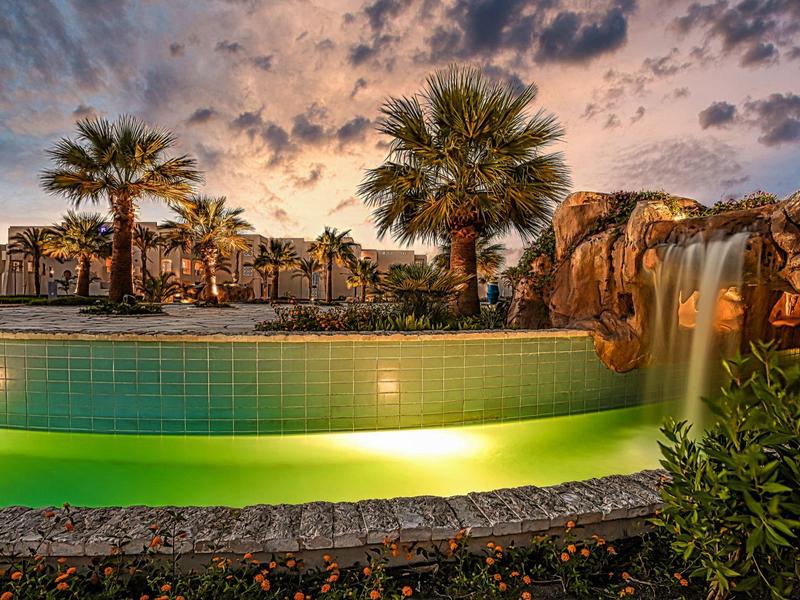 Illuminated pool with palm trees and rocks at sunset in tropical hotel resort