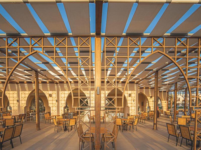 Open restaurant area with wooden framework and numerous tables and chairs in daylight.