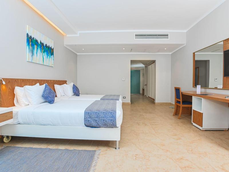 Bright hotel room with two beds, desk, and large mirror.