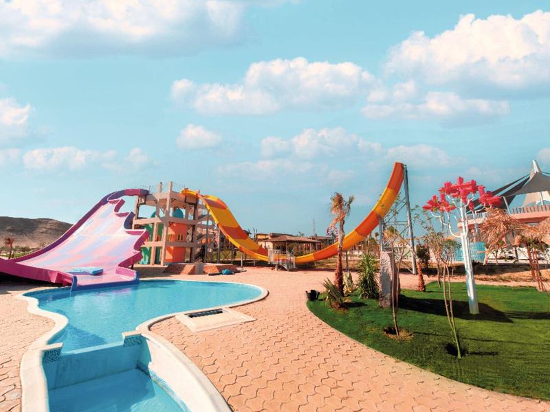 Bunter Wasserrutschenpark mit Pool, Pflasterweg, grünen Wiesen und blauem Himmel mit Wolken.