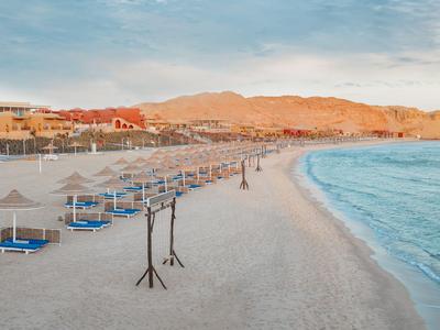 Spokojna piaszczysta plaża z leżakami i parasolami pod niebieskim niebem o zachodzie słońca.
