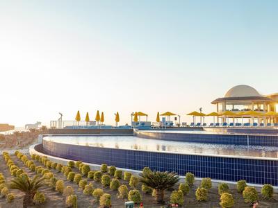 Nowoczesny basen na świeżym powietrzu z niebieskimi kafelkami obok budynku z kopułą pod bezchmurnym niebem.