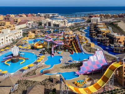 Bunter Wasserpark mit Rutschen, Pools und Gebäuden am Meer unter blauem Himmel.