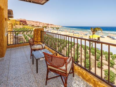 Taras z wiklinowymi krzesłami i widokiem na morze oraz słoneczną plażę.