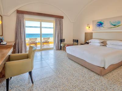 Geräumiges Hotelzimmer mit Doppelbett, Schreibtisch und Balkon mit Meerblick.