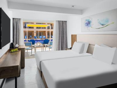 Nowoczesny pokój hotelowy z dwoma łóżkami, telewizorem i tarasem z widokiem na basen.