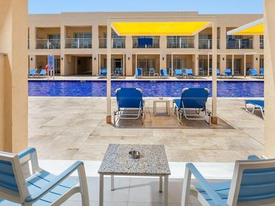 Taras hotelowy z basenem, niebieskie leżaki i widok na jasne pokoje.