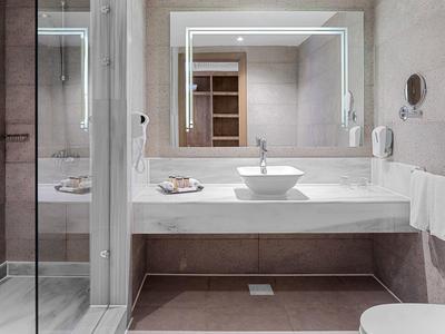 Nowoczesna łazienka z kwadratową umywalką, dużym podświetlanym lustrem i przeszkloną kabiną prysznicową.