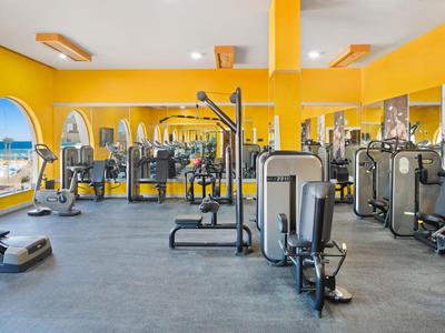 Dobrze wyposażona siłownia z żółtymi ścianami i dużymi lustrami.