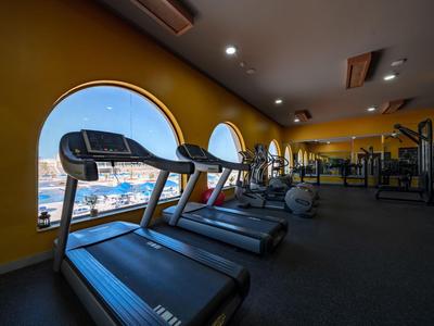 Siłownia z bieżniami i dużymi okrągłymi oknami z widokiem na marinę.