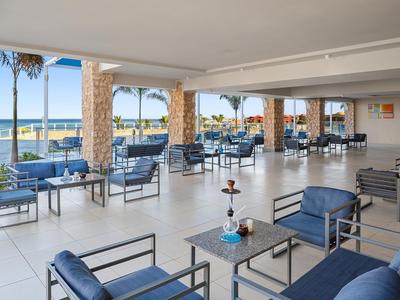 Otwarte miejsce do siedzenia z niebieskimi fotelami z widokiem na morze i palmy.