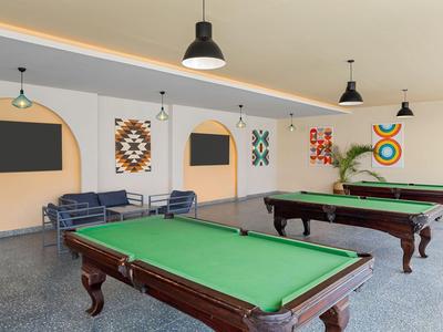 Duże pomieszczenie z kilkoma stołami bilardowymi, miejscami do siedzenia, obrazami na ścianach i lampami wiszącymi