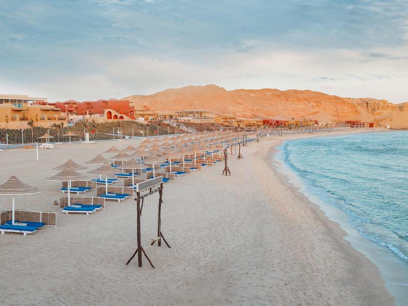 Spokojna plaża z leżakami, parasolami i niebieskim morzem o zachodzie słońca.