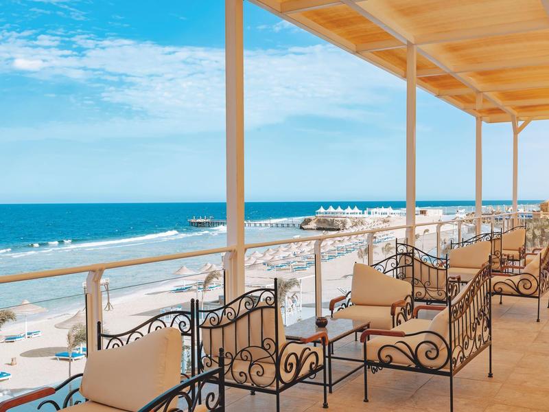 Taras hotelowy z żelaznymi fotelami z widokiem na morze i słoneczną plażę.