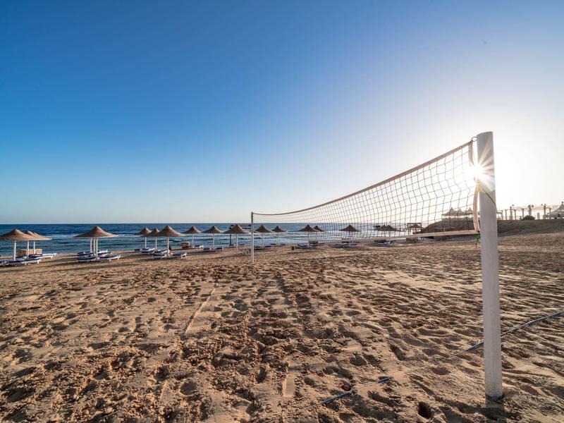 Piaszczysta plaża z siatką do siatkówki plażowej, parasolami i jasnym niebem o zachodzie słońca.