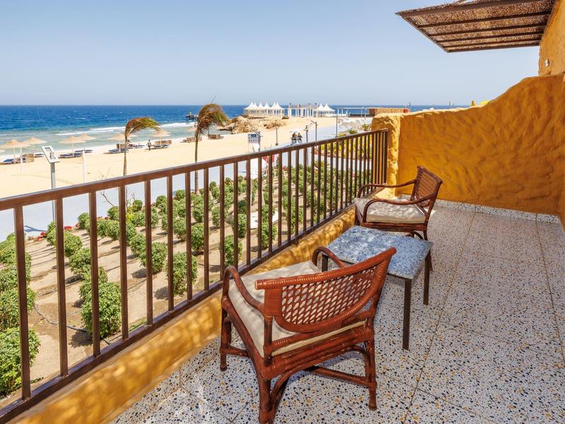 Balkon z dwoma krzesłami z widokiem na plażę i morze pod jasnym niebem.