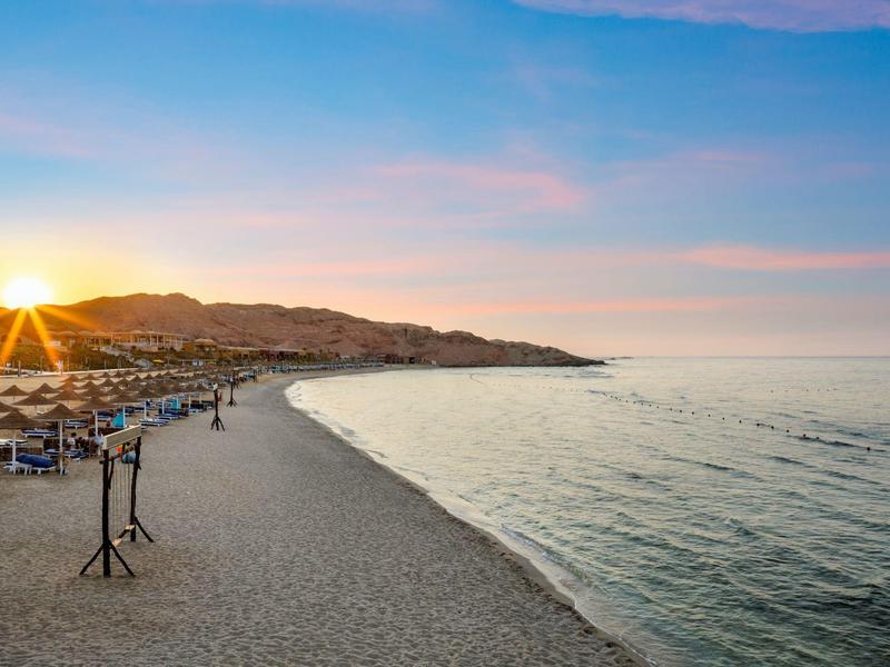 Plaża o zachodzie słońca z parasolami i spokojnym morzem.