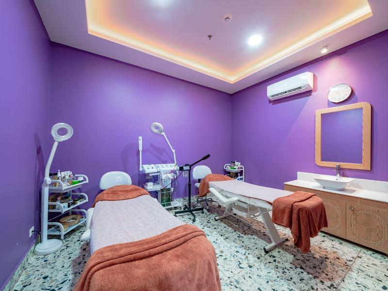 Fioletowy pokój spa z dwoma leżankami do masażu i ciepłym oświetleniem.