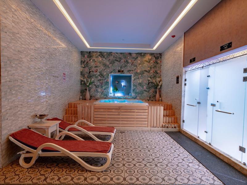 Strefa spa z dwoma czerwonymi leżakami, sauną i ozdobną kamienną ścianą.