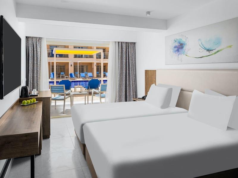 Nowoczesny pokój hotelowy z dwoma łóżkami, telewizorem i tarasem z widokiem na basen.