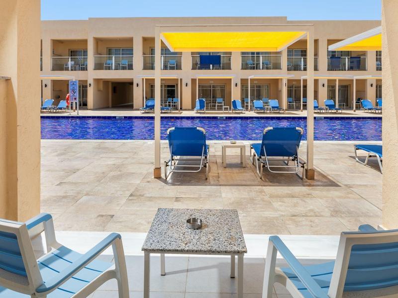 Taras hotelowy z basenem, niebieskie leżaki i widok na jasne pokoje.