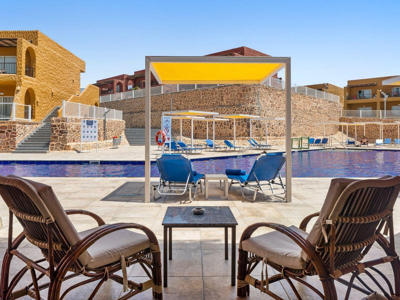 Taras z krzesłami i żółtym parasolem przy basenie w ośrodku hotelowym.