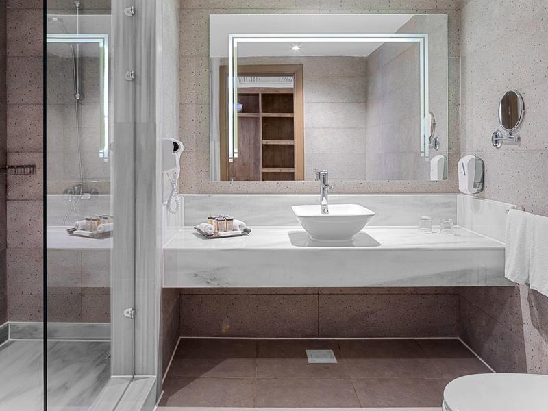 Nowoczesna łazienka z kwadratową umywalką, dużym podświetlanym lustrem i przeszkloną kabiną prysznicową.