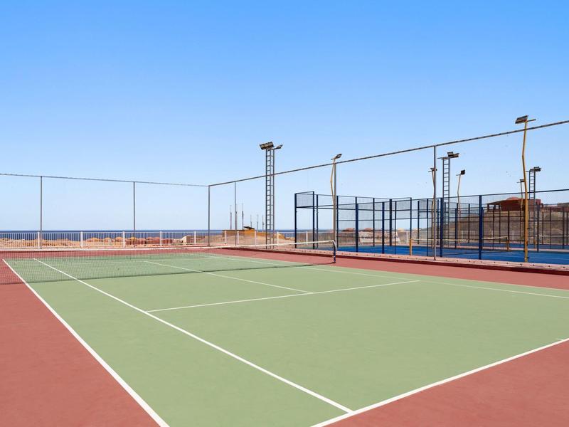 Zewnętrzny kort tenisowy z jasnym niebem i ogrodzeniem.