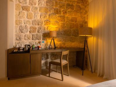 Un escritorio con silla, lámparas y pared de piedra en una habitación de hotel con luz cálida.