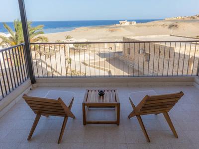 Balcón con dos sillas de madera y mesa pequeña con vista a la playa de arena y el mar.