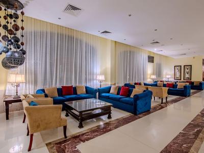 Salotto moderno di un hotel con divani blu, poltrone e grandi finestre con tende chiare.