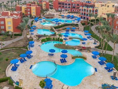 Blick auf mehrere geschwungene Hotelpools mit blauen Sonnenschirmen und umgeben von bunten Gebäuden.