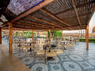 Überdachte Terrasse mit Metalltischen und Stühlen auf gemustertem Boden, umgeben von Pflanzen.